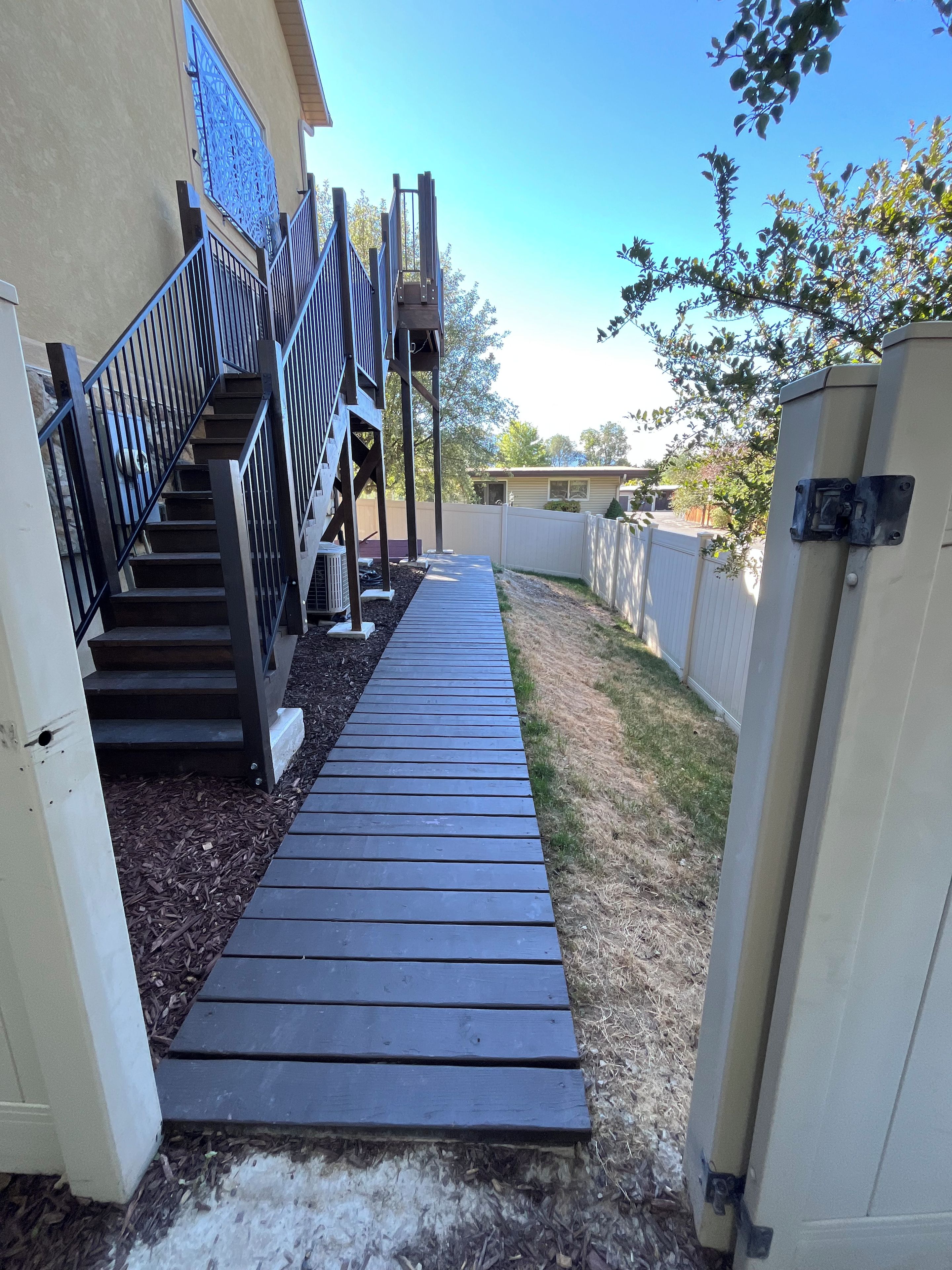 A wooden deck leading to a house with a metal staircase and a decorative metal gate.