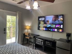 A hotel room with a bed, a desk with a lamp, a television mounted on the wall, and a minibar. - Convenient and private studio with relaxing deck (Holladay)