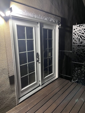 A double door with a frosted glass panel, a metal handle, and a white frame, set against a textured wall with a wooden deck in front. - Convenient and private studio with relaxing deck (Holladay)