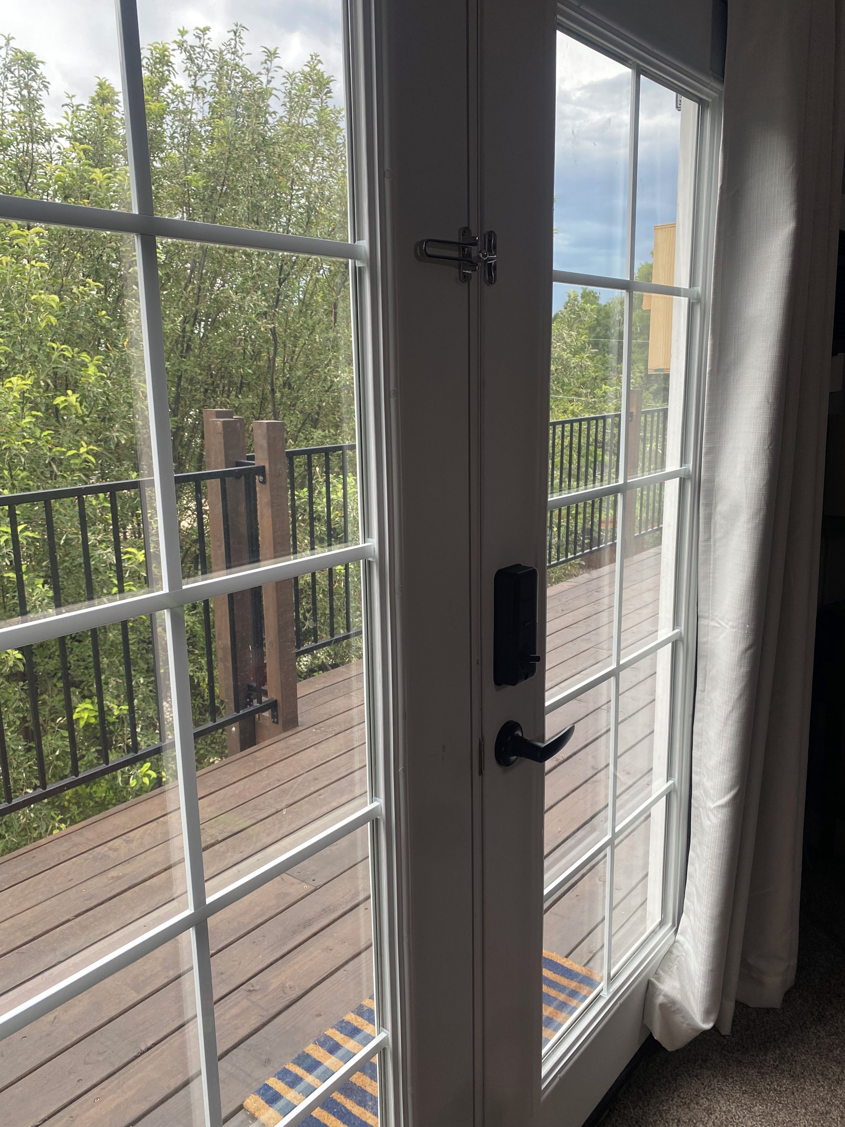 Blick aus einem Zimmer mit einem großen Glasfenster, das auf eine Terrasse mit Holzboden und Metallgeländer führt.