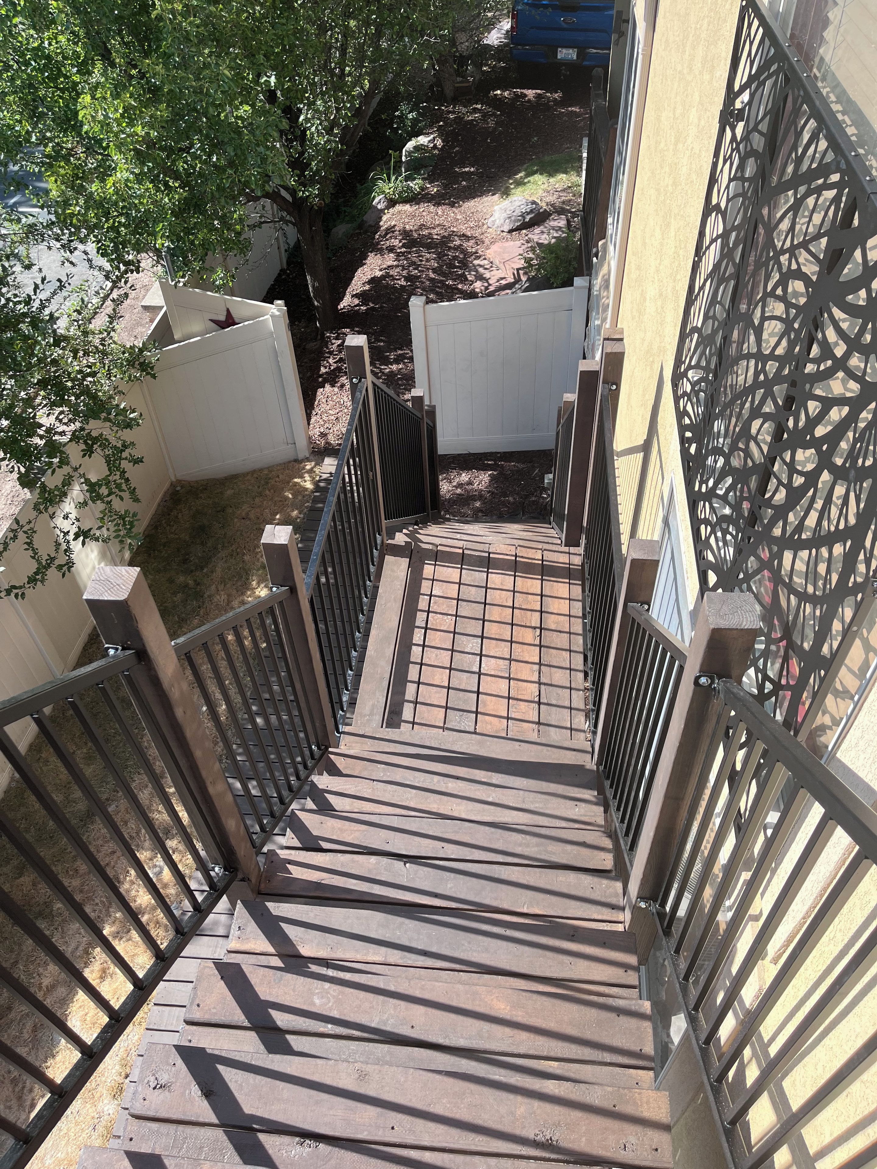 A wooden staircase with metal railings leading to a gated area with a white fence.