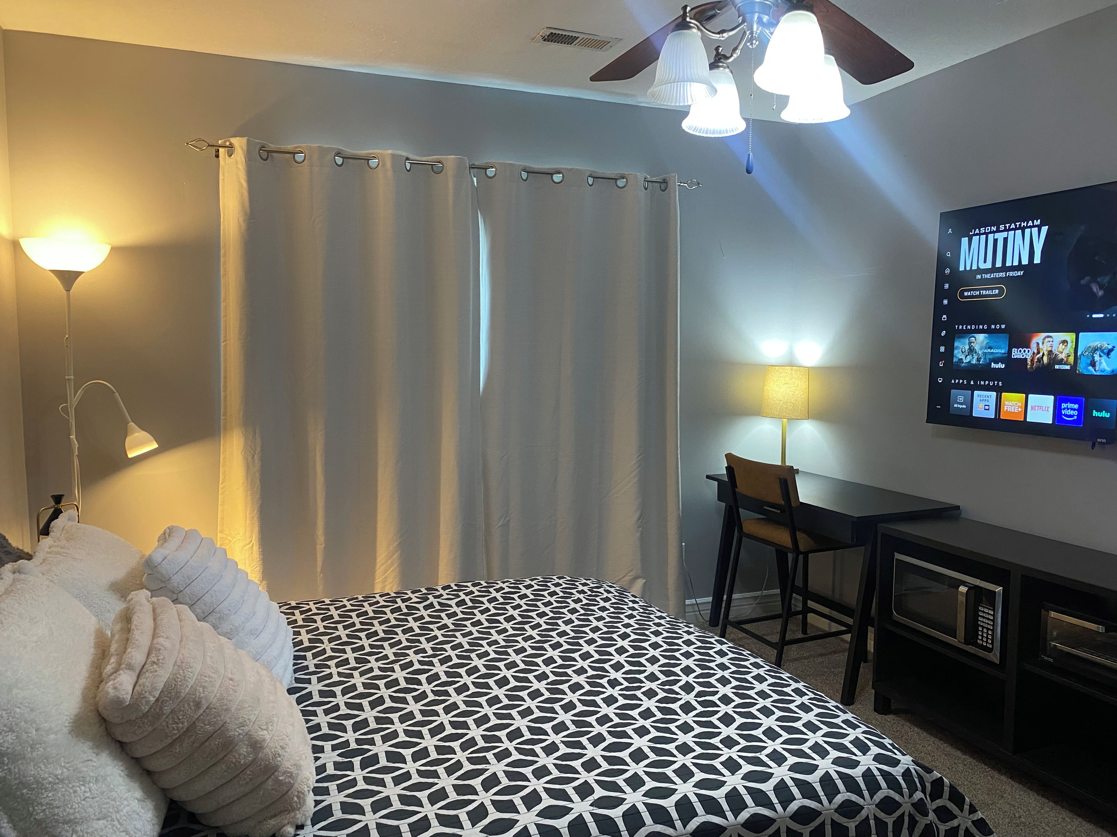 Ein Hotelzimmer mit einem Bett, einem Schreibtisch, einem Fernseher, der einen Film zeigt, und einem Deckenventilator.
