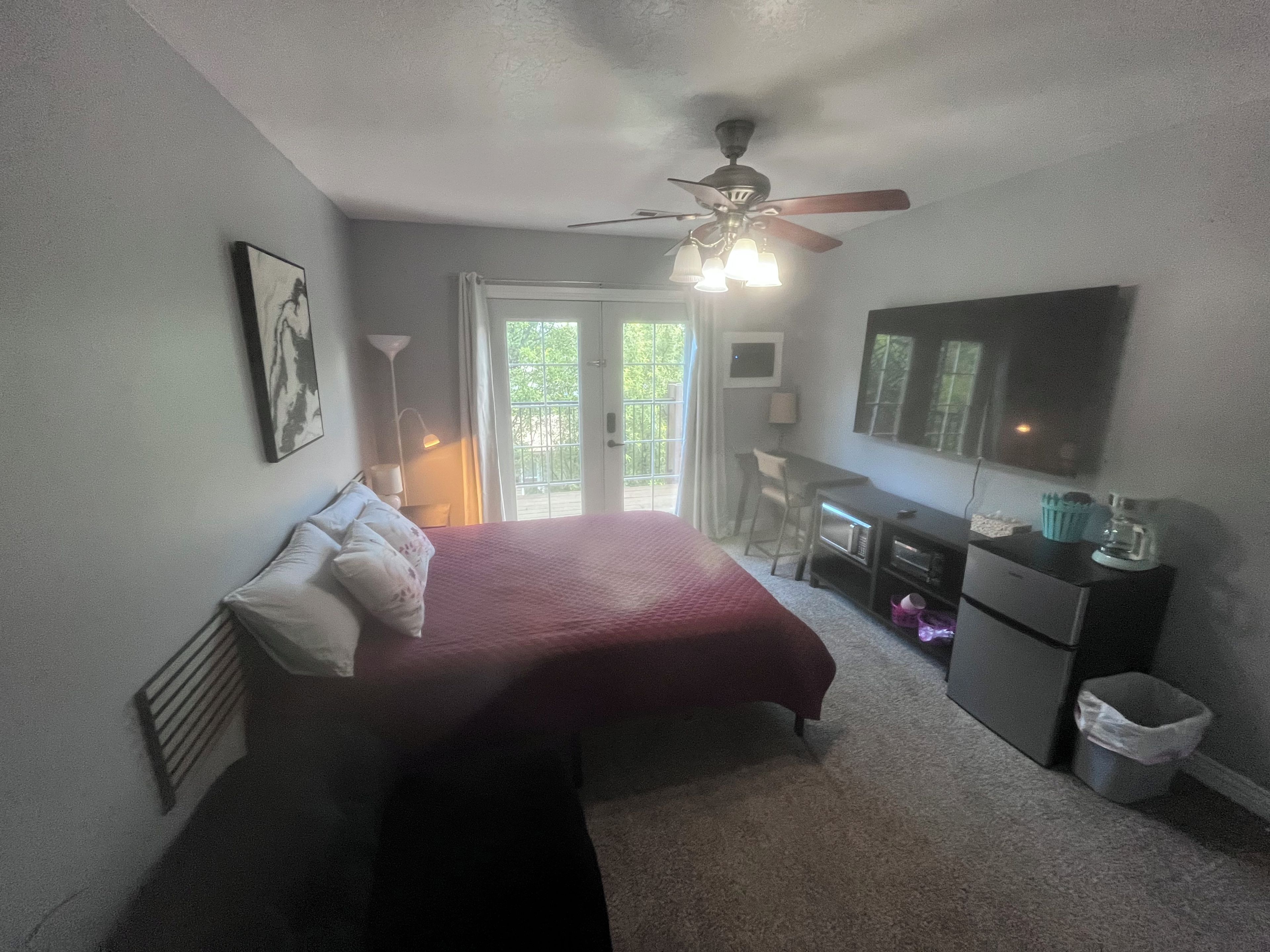 Ein Schlafzimmer mit einem Bett, einem Schreibtisch, einem Stuhl, einem Deckenventilator und einem Fernseher.