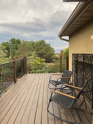 A wooden deck with two lounge chairs and a metal fence. - Convenient and private studio with relaxing deck (Holladay)