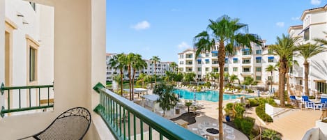 A balcony with a view of a pool area, lounge chairs, and palm trees.