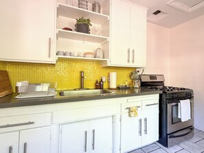 A kitchen with white cabinets, a yellow tiled backsplash, a stainless steel sink, a stove, and a countertop with various kitchen items. - Canyon Hill Retreat: Washer, Dryer, Full Kitchen, Patio, Private (Los Angeles)