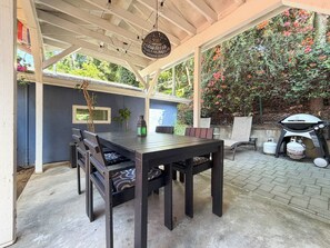 An outdoor patio with a wooden table and chairs, a hanging light fixture, and a grill. - Canyon Hill Retreat: Washer, Dryer, Full Kitchen, Patio, Private (Los Angeles)