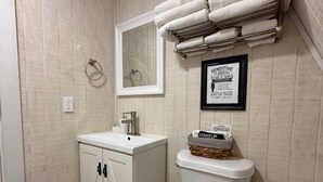 Een badkamer met een witte wastafel, een toilet, een handdoekhouder en een bord met tekst aan de muur.
