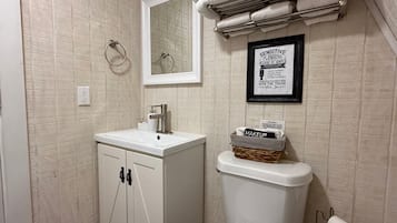 A bathroom with a white sink, a toilet, a towel rack, and a framed sign on the wall.
