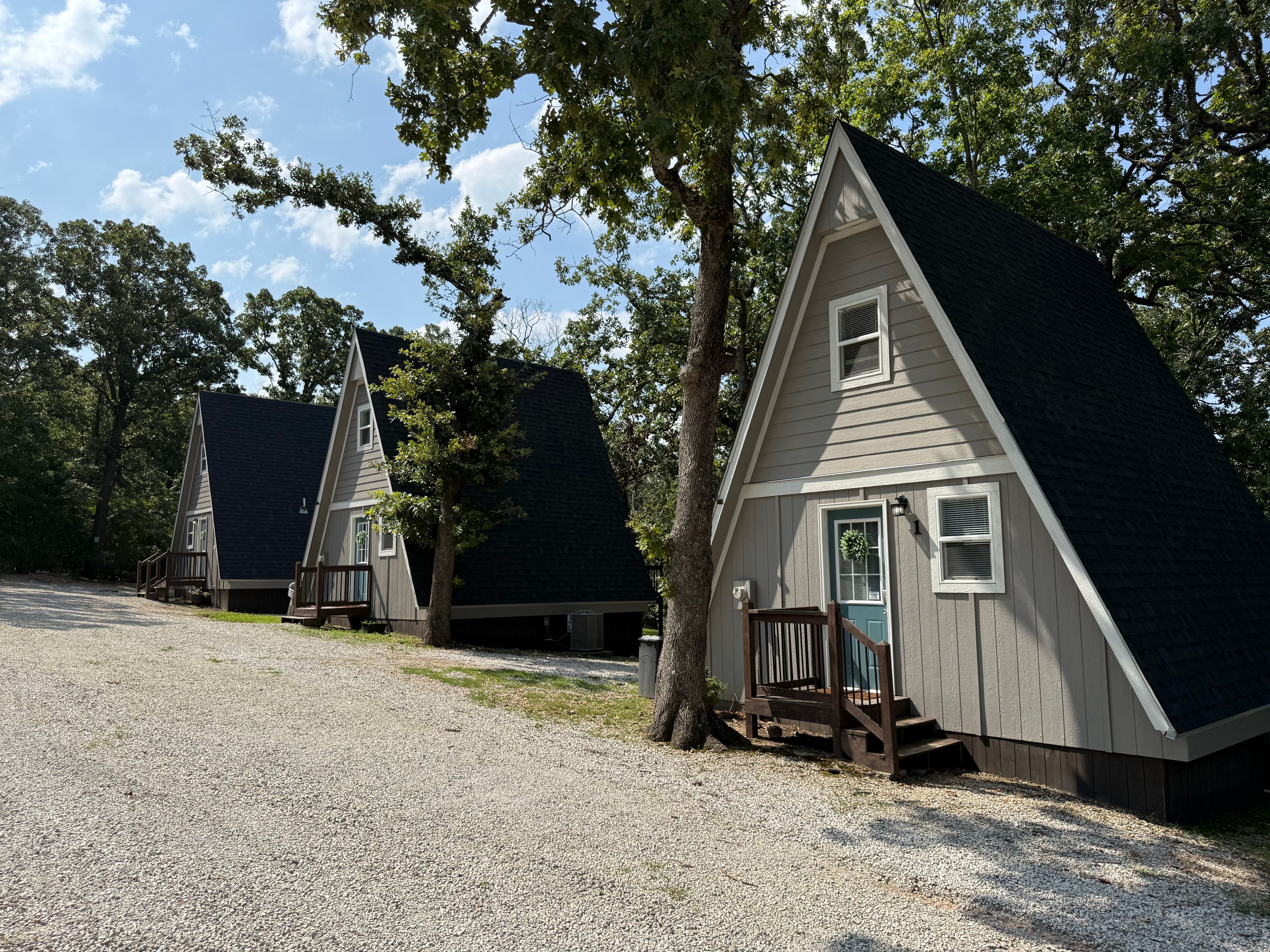 A row of small, triangular cabins with a gravel driveway and trees in the background.