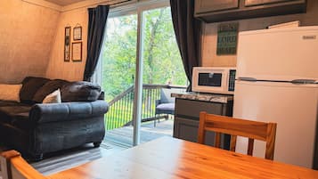 Un espacio habitable acogedor con sofá, una mesa de madera, una zona de cocina con refrigerador y microondas, y un ventanal corredero que da a una terraza.