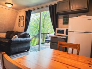 Un espacio habitable acogedor con sofá, una mesa de madera, una zona de cocina con refrigerador y microondas, y un ventanal corredero que da a una terraza.