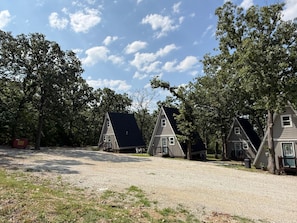 Een rij A-frame accommodaties met een grindpad en omliggende bomen.