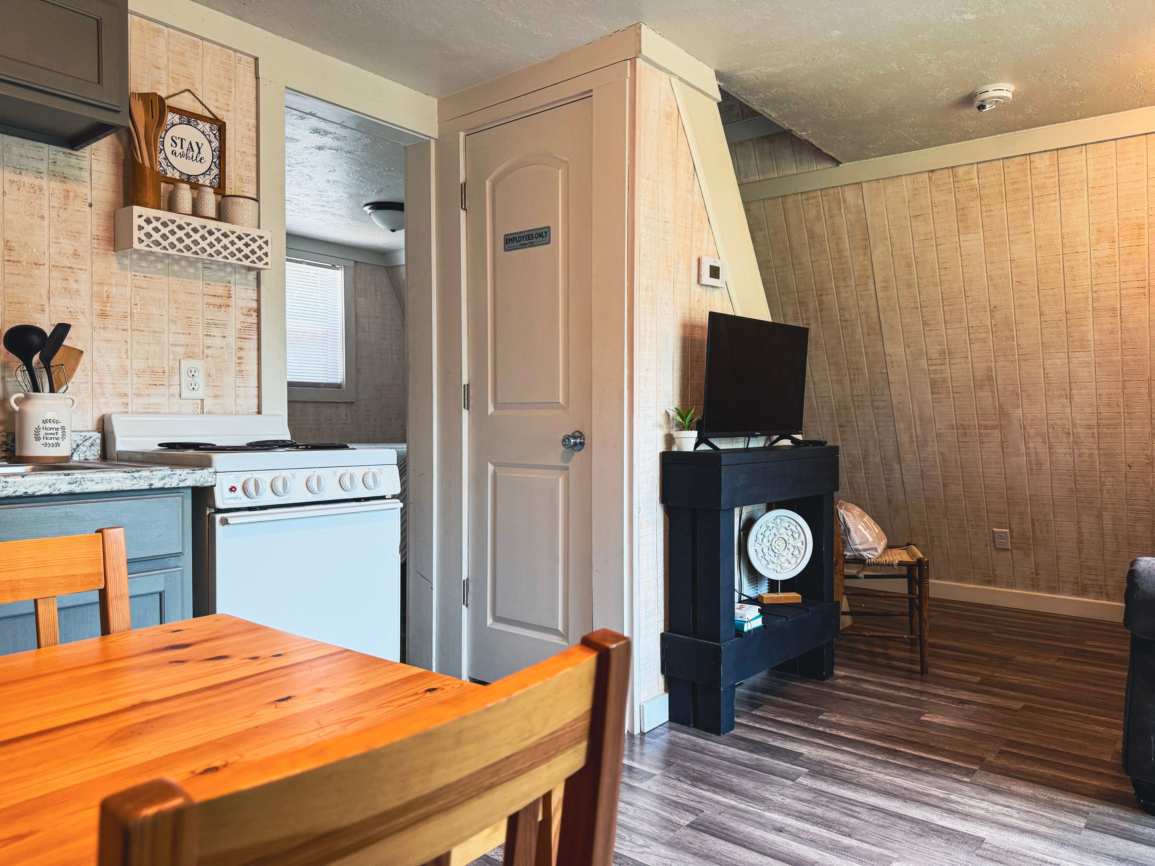 A kitchen with a stove, a dining table with chairs, a television on a stand, and a door marked 'EMPLOYEES ONLY'.