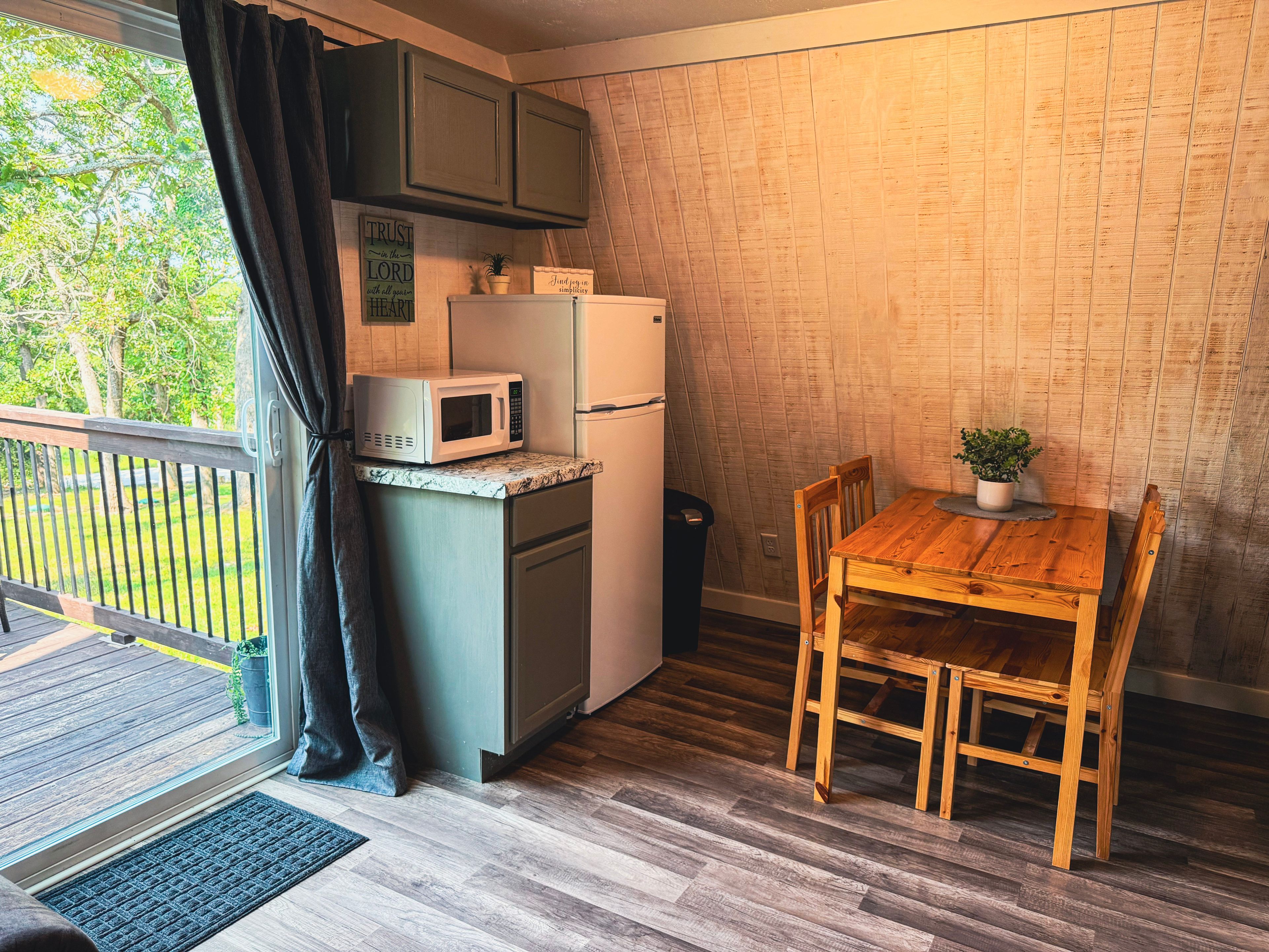 Cocina compacta equipada con microondas, refrigerador y mesa de madera con sillas.