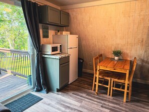Een kleine keuken met een magnetron, koelkast en een houten tafel met stoelen.