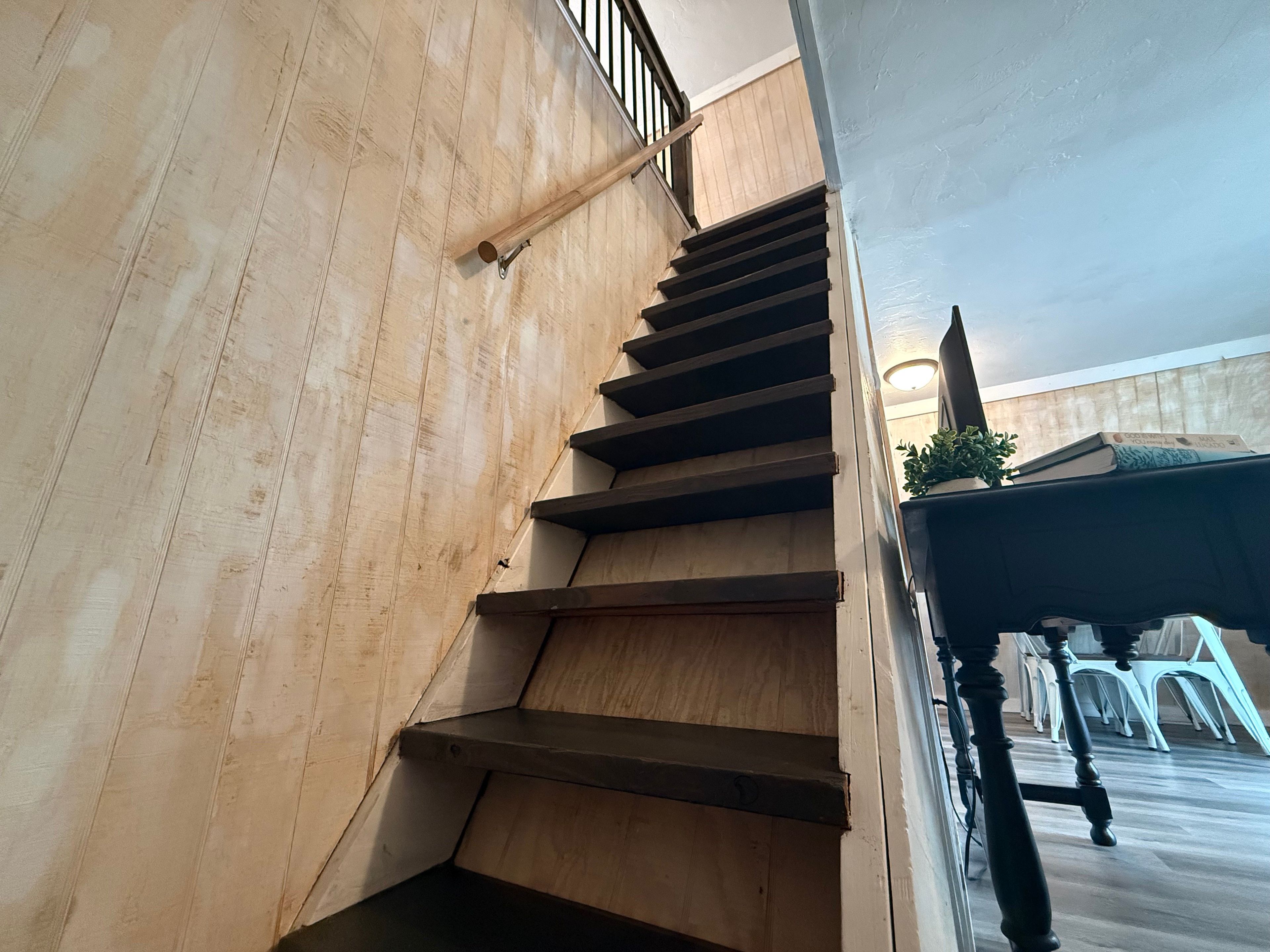 Una escalera de madera con barandilla de metal que conduce a una plataforma con una planta en maceta y una mesa con sillas.