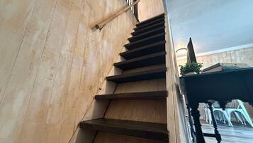 Una escalera de madera con barandilla de metal que conduce a una plataforma con una planta en maceta y una mesa con sillas.