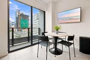 A modern room with a balcony, a round table with chairs, a potted plant, and a flat-screen TV on the wall. - Modern Miami Studio | 801B | Pool Hot Tub & Gym (Miami)