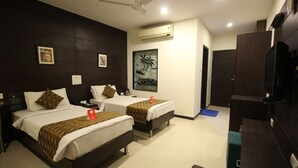 Een hotelkamer met twee bedden, een plafondventilator, een airconditioningapparaat, een schilderij aan de muur en een televisie op een standaard.