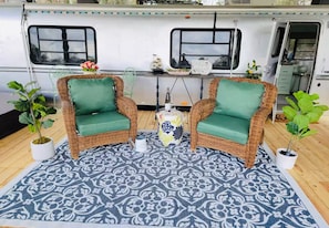 A cozy seating area with wicker chairs and a patterned rug, a small table with decorative items, and potted plants.