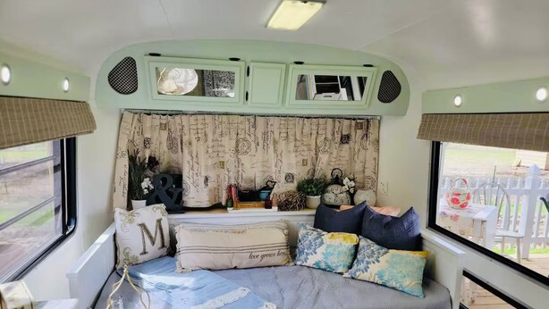 Een gezellig RV-interieur met een bed, opbergladen, een klein tafeltje en een raam met uitzicht op de natuur.