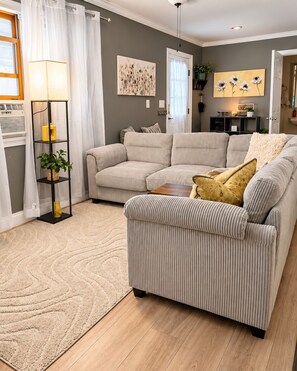 A living room with a sectional sofa, a floor lamp, a rug, and wall art. - Cozy & Quiet Country 1-Bedroom Stay with Private Living Room, Bath and Entrance (Elbridge)