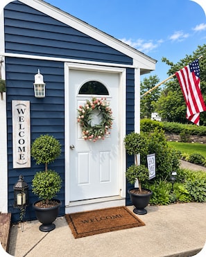A house with a white door, a welcome sign, a wreath, and an American flag.