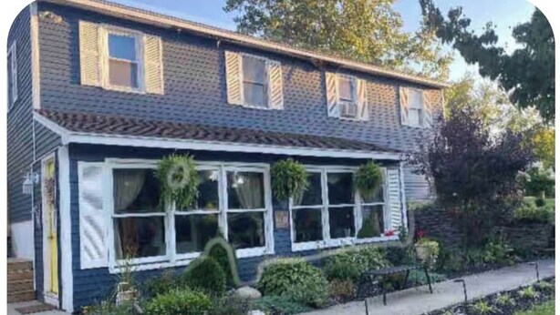 Une maison à deux étages avec un porche à l’avant, un petit jardin et un chemin menant à l’entrée.