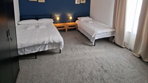 Una habitación con dos camas individuales, un armario, una lámpara en el techo e imágenes enmarcadas en la pared.