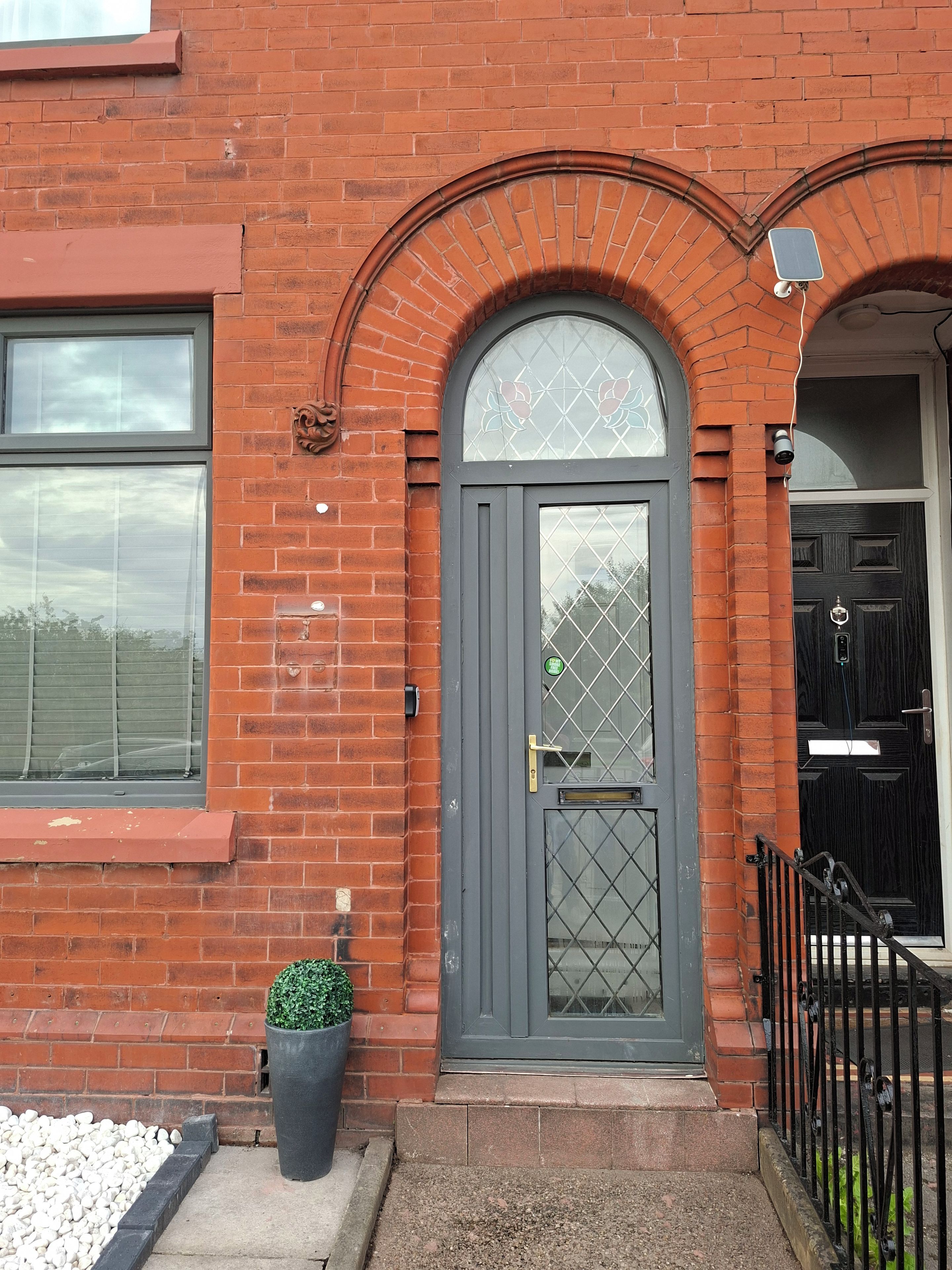 A brick building with a grey door, a small potted plant, and a metal fence.