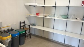 Une cuisine avec des étagères blanches, une chaise et des poubelles.