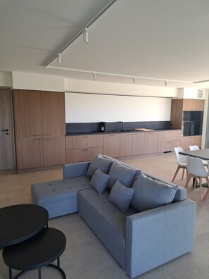 A modern kitchen with wooden cabinets, a grey sofa, and a dining area with white chairs.