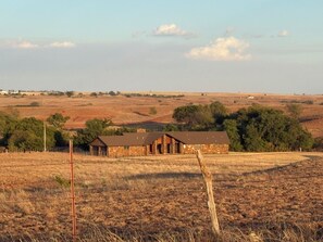 A stone building with a sloped roof, surrounded by a fenced property with dry grass and sparse trees.