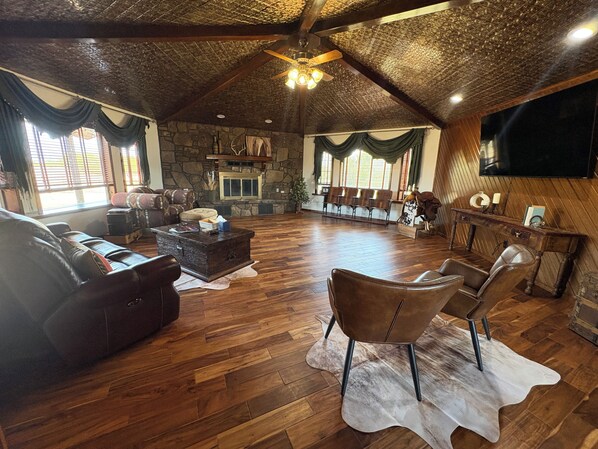 A spacious living area with a stone fireplace, leather furniture, and a wooden ceiling.