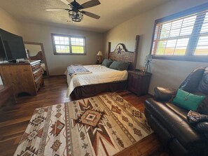 A bedroom with a bed, a dresser, a television, a window, and a ceiling fan.