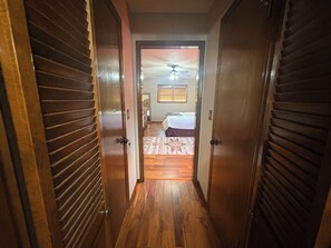 A hallway with wooden doors leading to a bedroom with a bed and a ceiling fan.