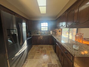 A kitchen with dark wooden cabinets, a stainless steel refrigerator, granite countertops, and a window providing natural light.