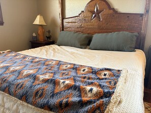 Una cama con una colcha estampada, un cabecero de madera con diseño de estrella y una mesita de noche con una lámpara y un objeto decorativo pequeño.