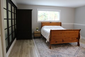 Un dormitorio con una cama de madera, una mesita de noche, una pequeña mesa con una planta y una ventana con persianas.