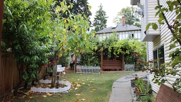 Un patio trasero residencial con valla de madera, cerca blanca de piquetes, banco de jardín y una variedad de plantas y árboles.
