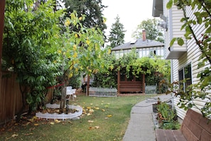 Un jardin à l’arrière d’une maison, avec une clôture en bois, une petite clôture blanche, un banc de jardin et une variété de plantes et d’arbres.