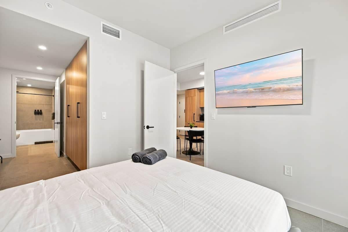 A modern bedroom with a large bed, a flat-screen TV, and a view of the beach.