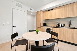 A modern kitchen with wooden cabinets, a round table with chairs, and a small potted plant. - Downtown Miami 1006| Rooftop Pool Hot Tub & Gym (Miami)