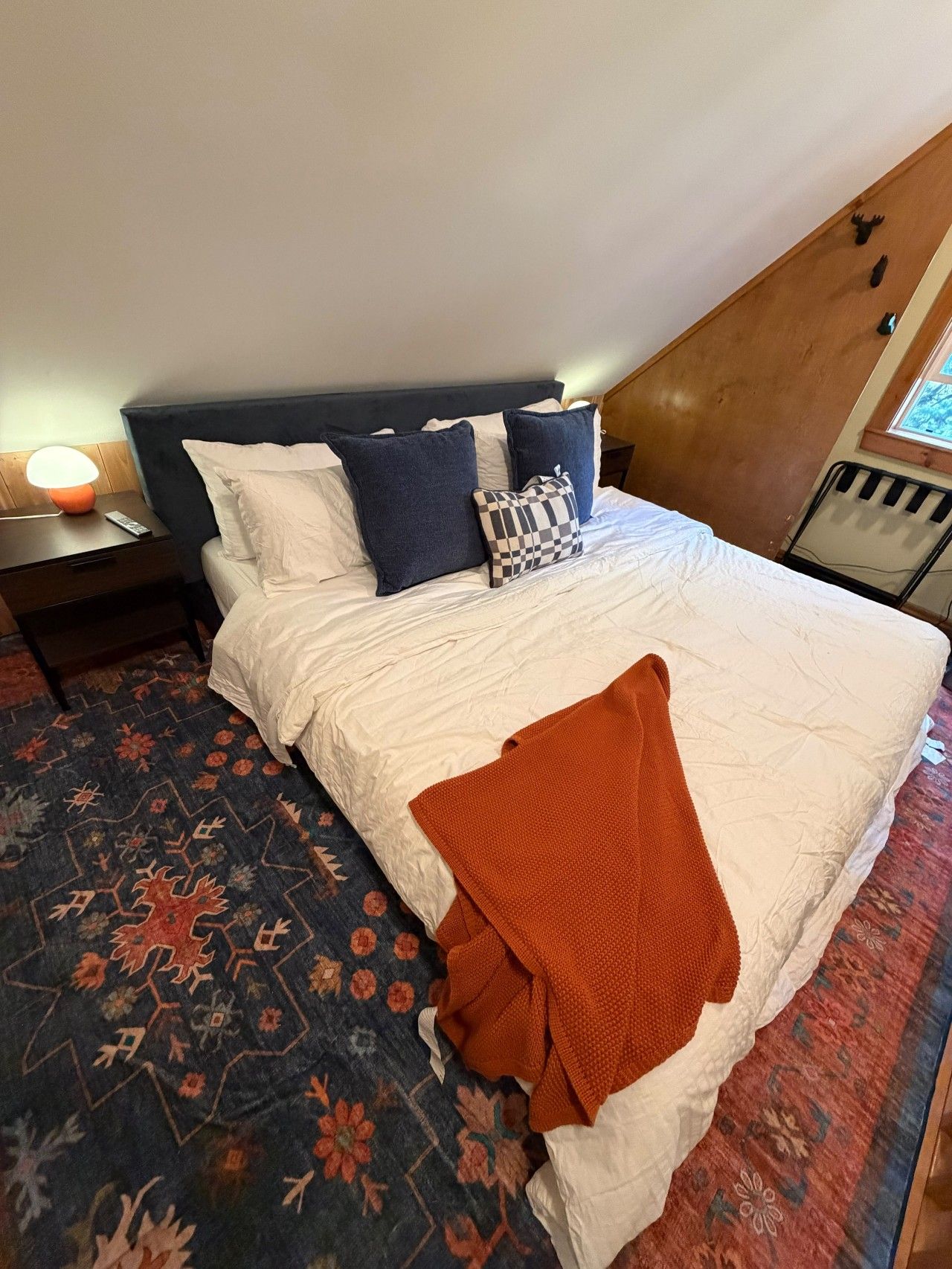 Ein Schlafzimmer mit einem Bett, Kissen, einer Decke, einem Nachttisch, einer Lampe und einem Fenster.