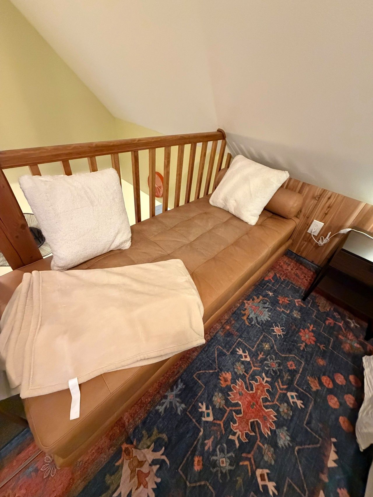A single bed with a wooden headboard, two pillows, a blanket, and a patterned rug.