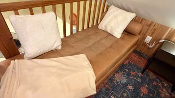 A single bed with a wooden headboard, two pillows, a blanket, and a patterned rug.