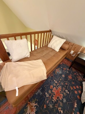 A single bed with a wooden headboard, two pillows, a blanket, and a patterned rug.