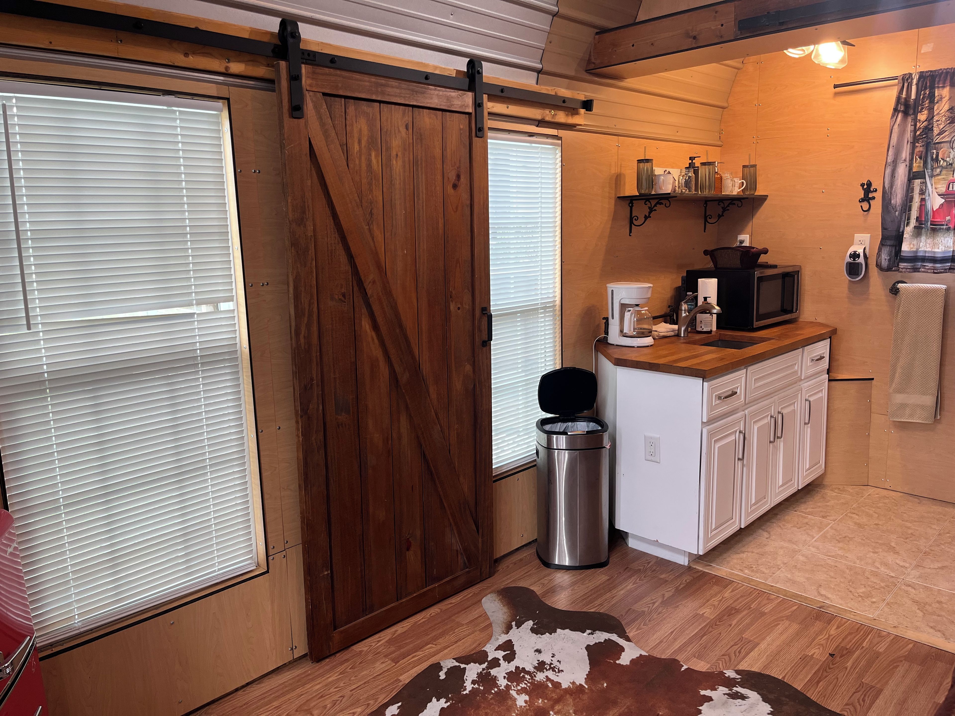 A compact kitchen with a sliding barn door, a coffee maker, a microwave, and a small trash bin.