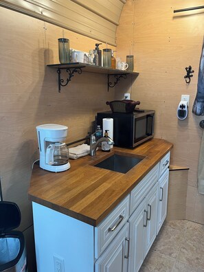 Une cuisine compacte équipée d’une machine à café, d’un four à micro-ondes et d’une étagère avec des bocaux.
